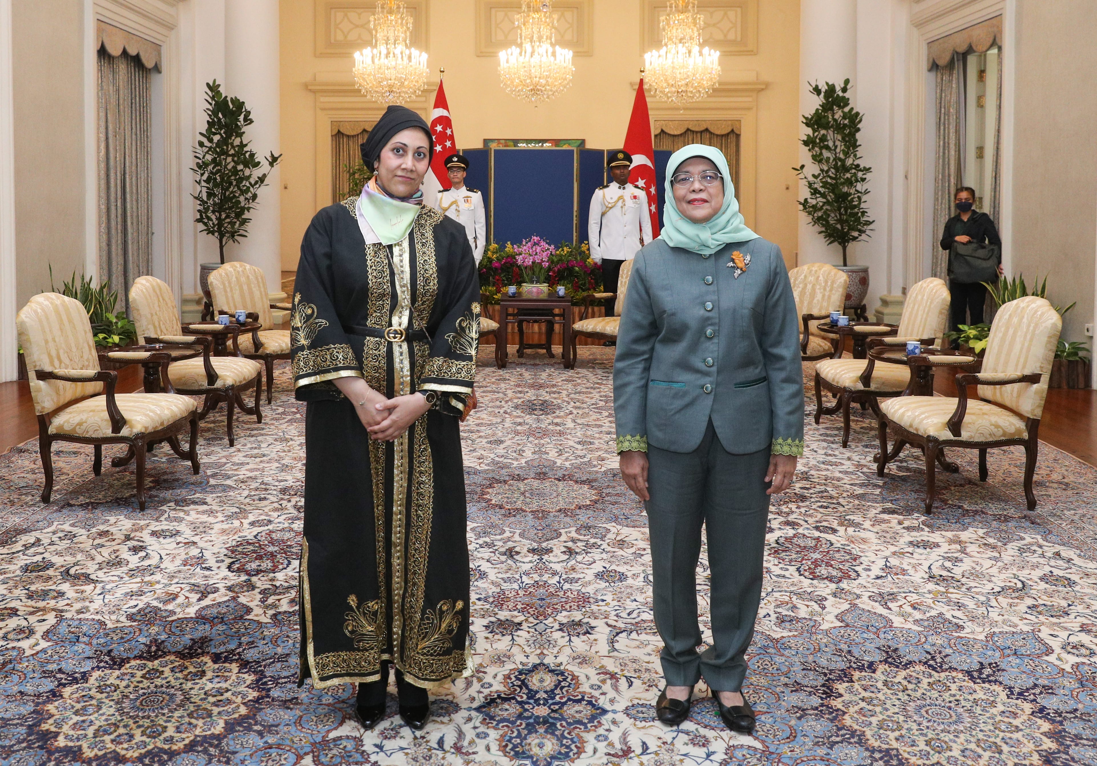 Two women in formal attire stand in a room with Singapore flags.